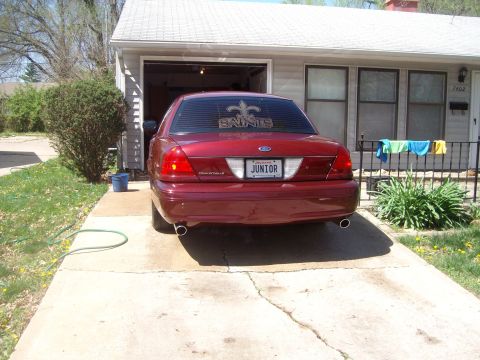 2004 Ford Crown Victoria - A red Ford Crown Victoria is parked in a driveway in front of a house with laundry hanging on a fence.