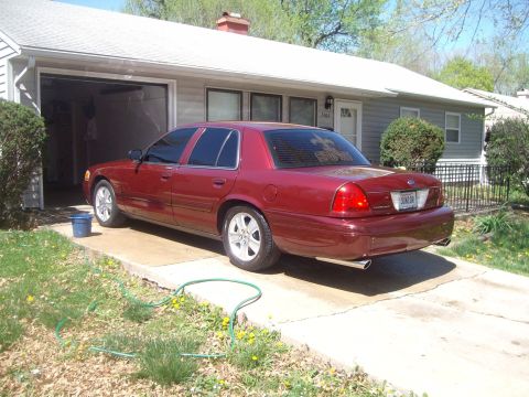 2004 Ford Crown Victoria - A red sedan is parked in a driveway in front of a house.