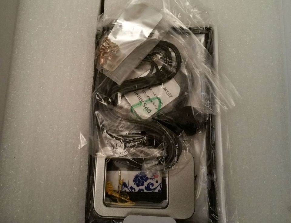 GPS antenna and cables in plastic packaging, with a decorative tin