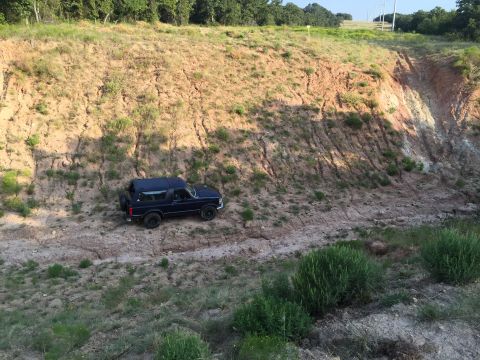 1993 Ford Bronco - A Ford Bronco is parked on a dirt path beside a large, eroded hill under a clear sky.