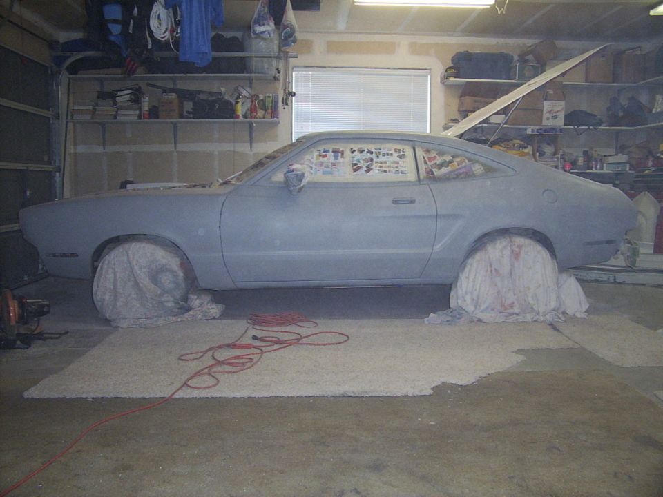 Primer-gray hatchback coupe on jack stands in a garage during bodywork