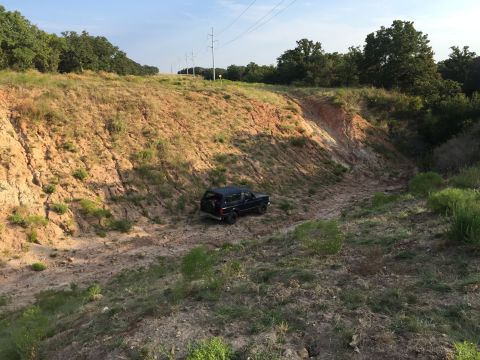 1993 Ford Bronco - A black SUV is positioned on a dirt path within a dry creek bed, surrounded by eroded hills and vegetation.