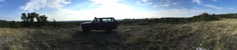 1993 Ford Bronco - A Ford Bronco sits in a field with trees and hills in the background under a bright sky.