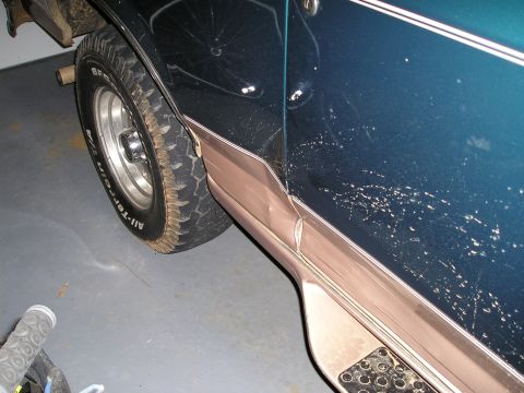 1996 Ford Bronco - The side of a dark teal 1992 Ford Bronco with damaged trim and paint is visible.
