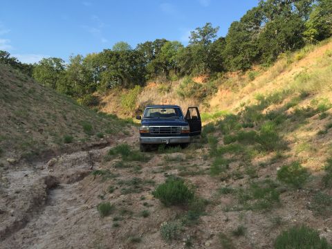 1993 Ford Bronco - A dark blue 1993 Ford Bronco is parked in a dirt ravine with the driver's door open under a clear blue sky.