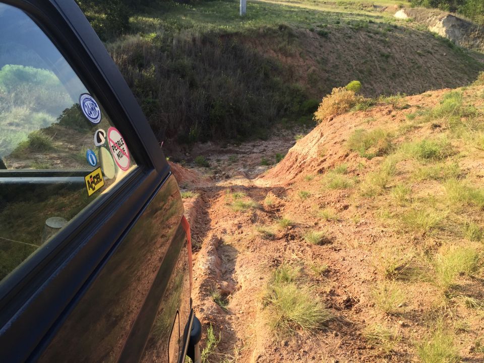Side view of a dark SUV on a muddy off-road trail with grass and dirt hills