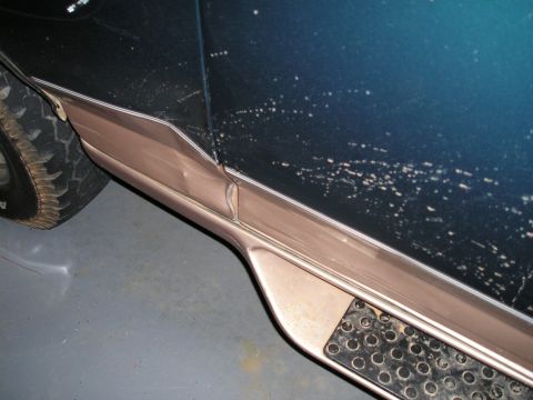 1996 Ford Bronco - The side panel and running board of a dark blue SUV show damage to the trim.
