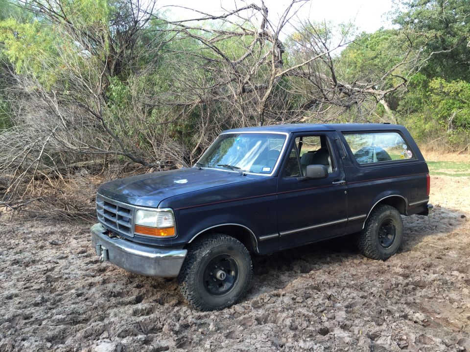1993 Ford Bronco parked on muddy ground with trees in background