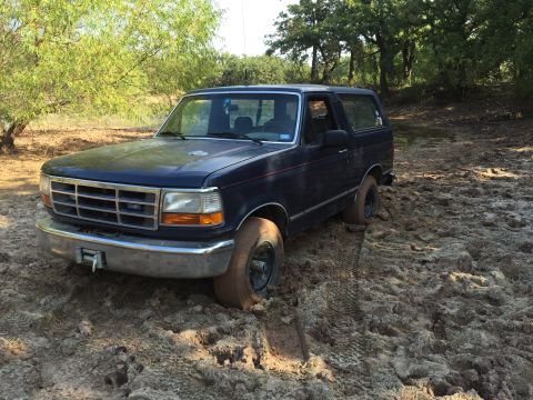 1993 Ford Bronco - This dark blue 1993 Ford Bronco is stuck in a muddy area with trees in the background.