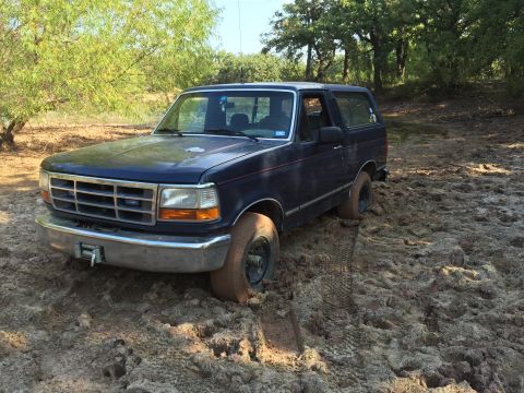 1993 Ford Bronco - This 1993 Ford Bronco is stuck in a muddy area with trees in the background.