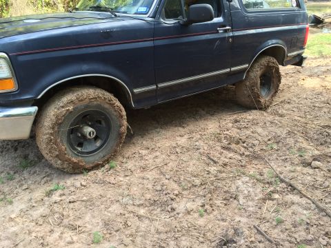 1993 Ford Bronco - The side view of a dark blue Ford Bronco stuck in thick mud. The front and rear tires are caked with mud, with the rear tire appearing to b…