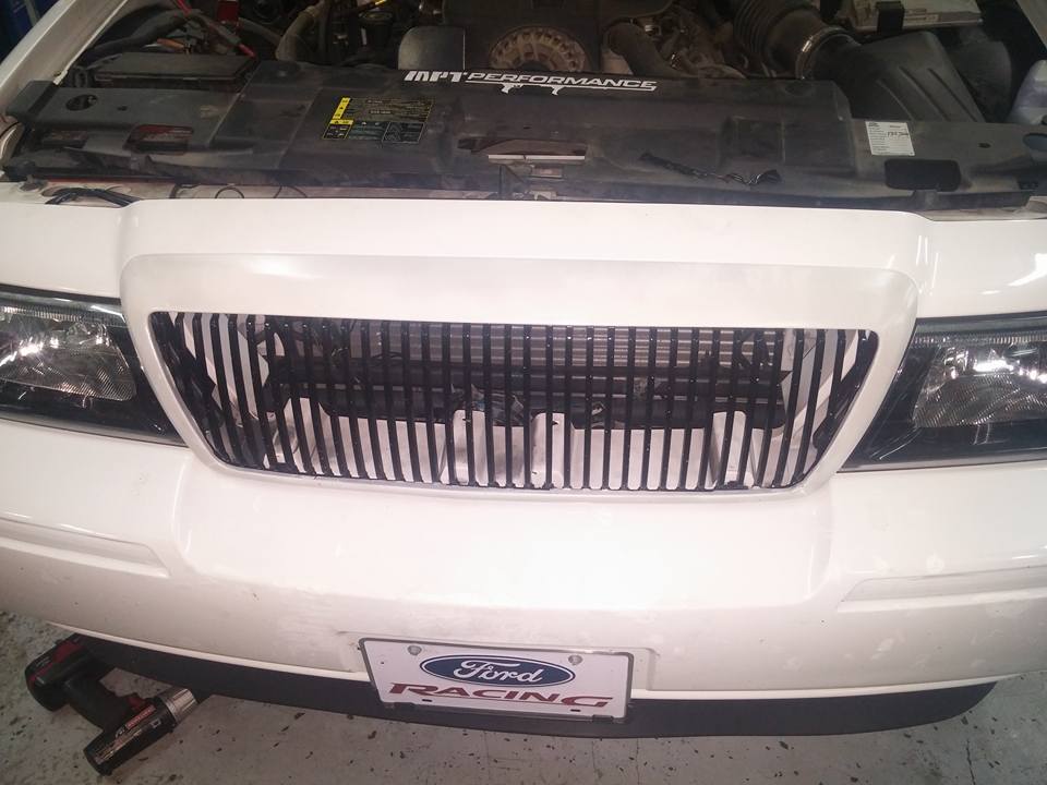 Front grille and engine bay of a white sedan in a garage