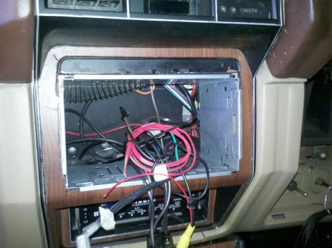 1982 Ford Bronco - The interior of a vehicle shows a car stereo mounting bracket with various wires connected to it. Below the bracket, a climate control pane…