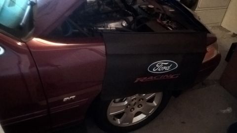 2004 Ford Crown Victoria - A Ford Racing fender cover is visible on the side of a maroon vehicle, partially obscuring the wheel and engine bay.