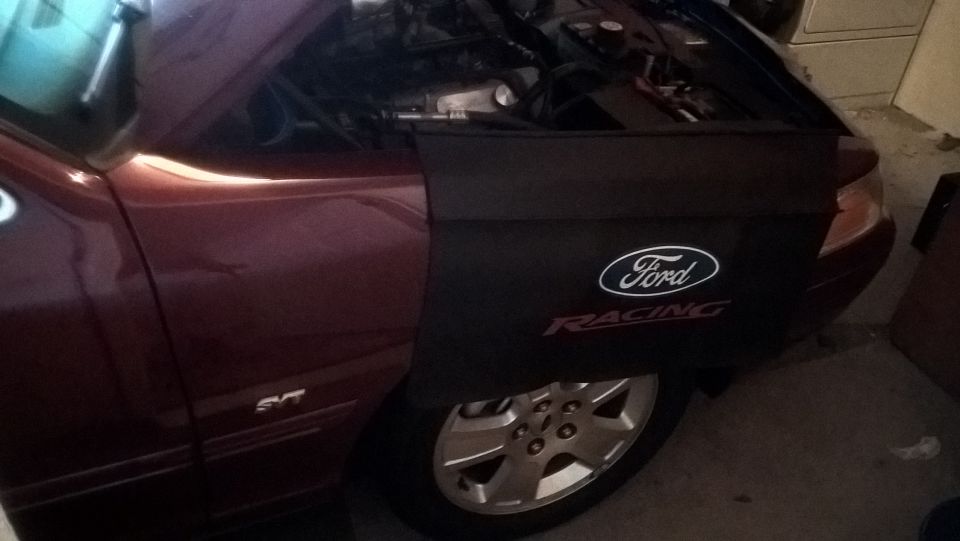 Ford Racing fender cover over the front fender of a dark red sedan with the hood open