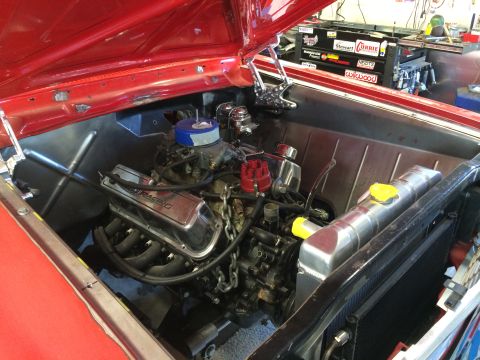 1964 Ford Fairlane - The engine bay of a red car is shown, chrome valve covers and a blue air filter, with a toolbox in the background.