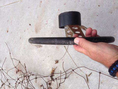 1979 Ford Bronco - A part of a steering wheel is held up against a concrete surface with some wire debris in the foreground.