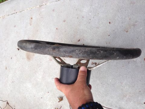1979 Ford Bronco - A steering wheel part is held by a hand against a concrete surface.