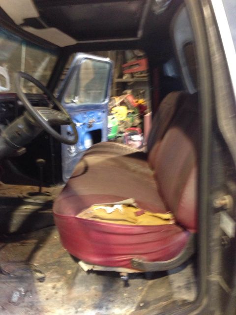 1979 Ford Bronco - The interior of a vehicle shows worn seats and an open door, with tools in the background.