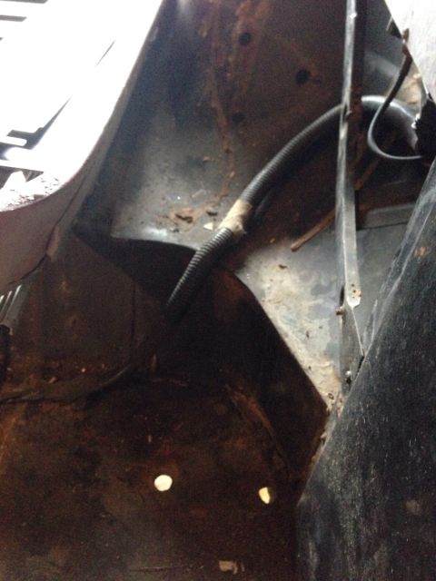 1979 Ford Bronco - Close-up view of a rusty interior fender well with a black hose running through it.