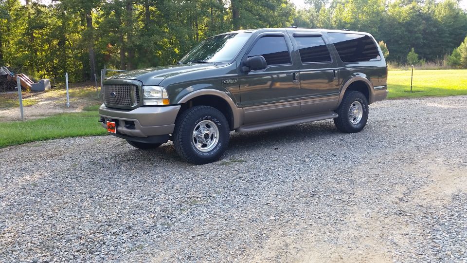 Green Ford Excursion parked on gravel lot, trees in background