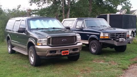 2003 Ford Excursion - Two Ford SUVs, a 2003 Excursion and a Bronco, are parked on a grassy area next to a trailer.