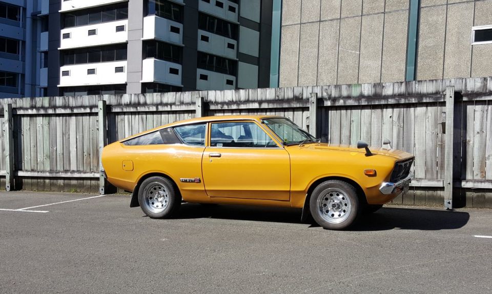 Yellow Datsun coupe parked outside a building, side view