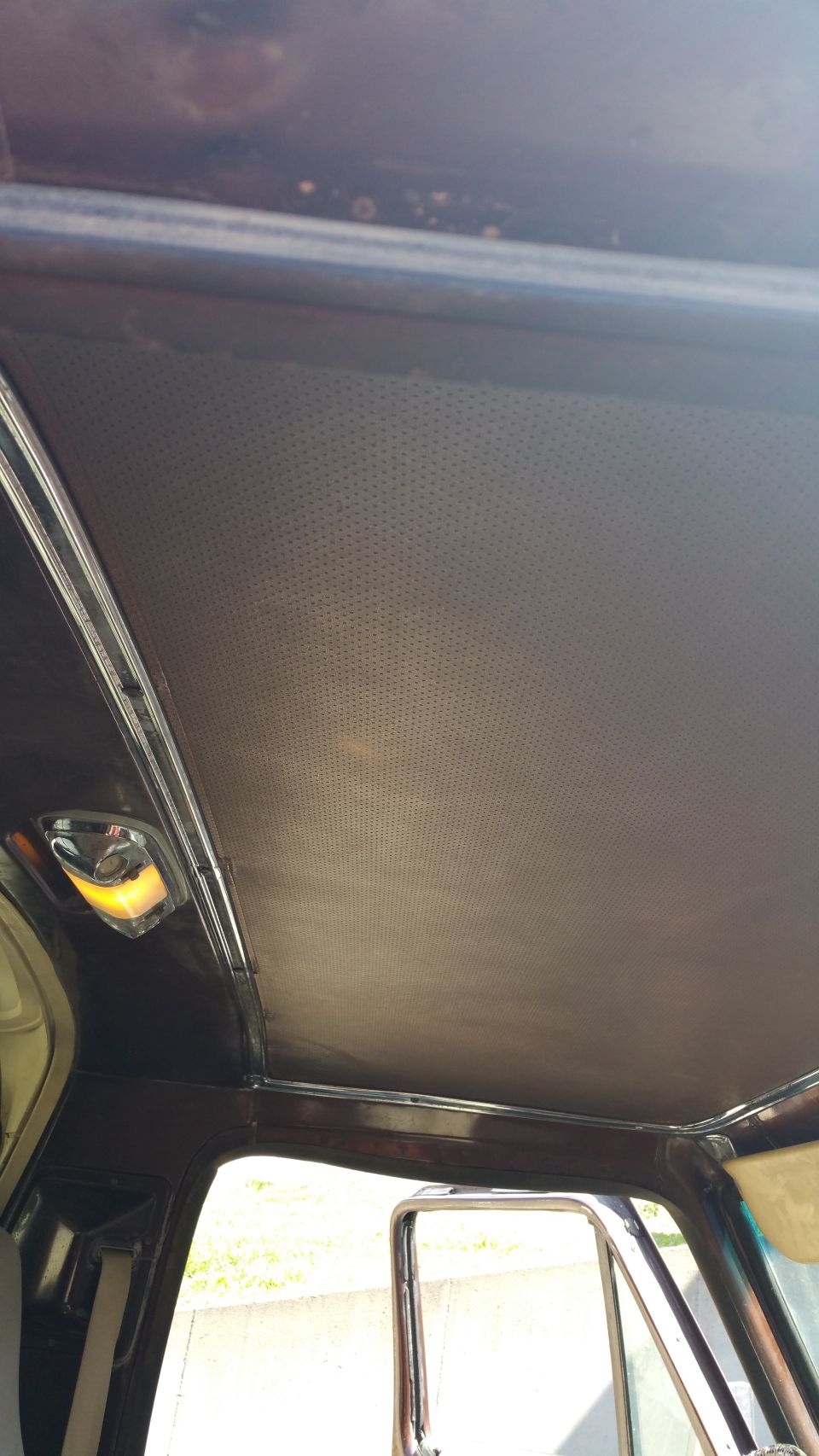 Vehicle interior ceiling with perforated headliner and dome light. Visible door frame and mirror