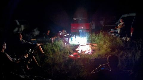 1996 Ford Bronco - People gather around a campfire at night, with multiple vehicles present in the dimly lit surroundings.
