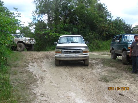 1996 Ford Bronco - A white Ford F-Series truck navigates a muddy off-road path alongside other vehicles.
