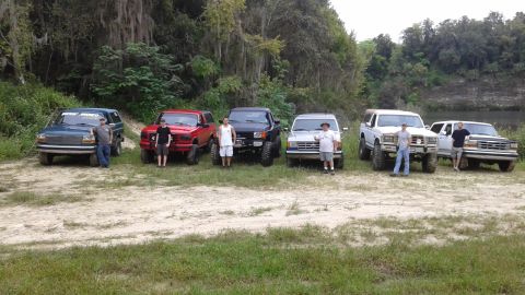1996 Ford Bronco - Several SUVs and trucks are lined up in a scenic outdoor location, with a white Ford Bronco among them.
