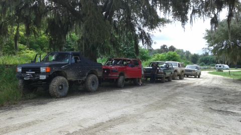 1996 Ford Bronco - Several SUVs, including a 1996 Ford Bronco, are parked on a dirt road in a wooded area.