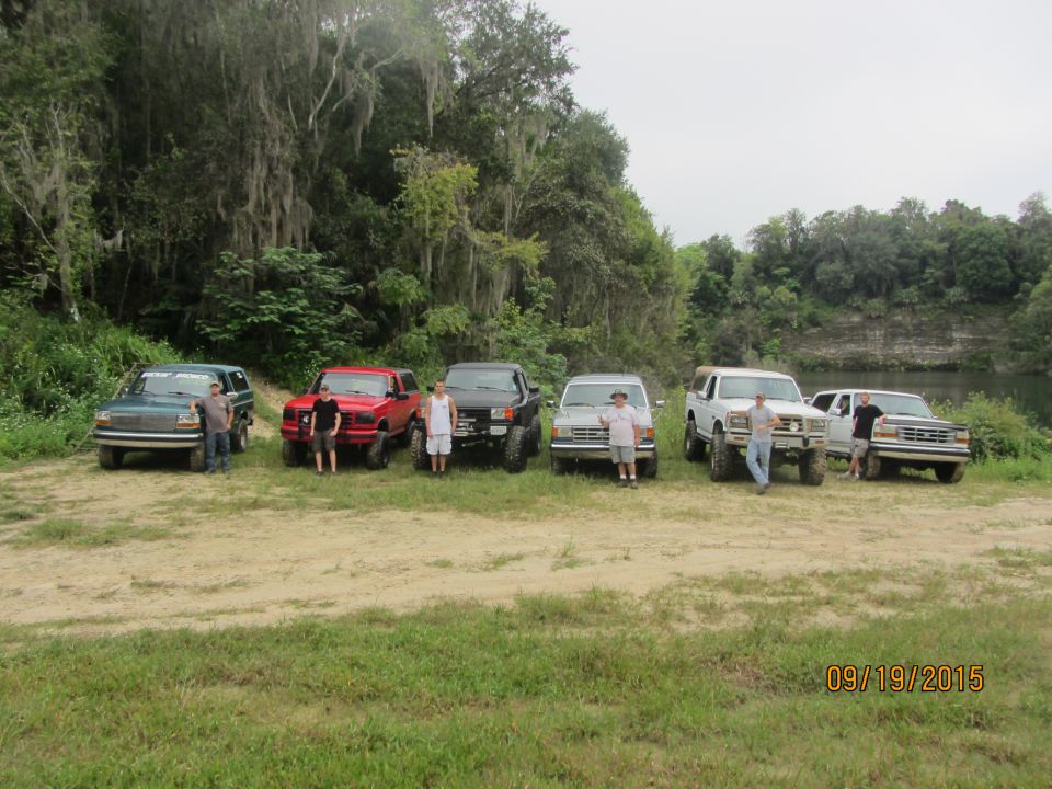 Six trucks and SUVs parked in a line with people standing by them. The vehicles appear to be from the 1990s