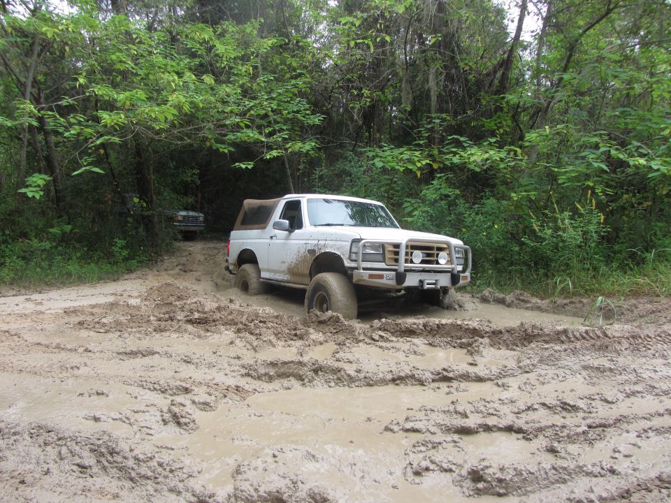 White 1992 Ford Bronco stuck in mud on a wooded trail