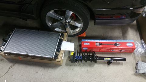 2002 Chrysler 300M - New parts including a radiator, CV axle, and strut assembly are laid out on the ground next to a car's wheel.