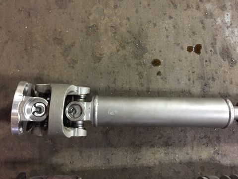 1995 Ford Bronco - A driveshaft with universal joints and a flange is shown against a concrete floor. The Supermotors.net logo is visible in the lower right c…