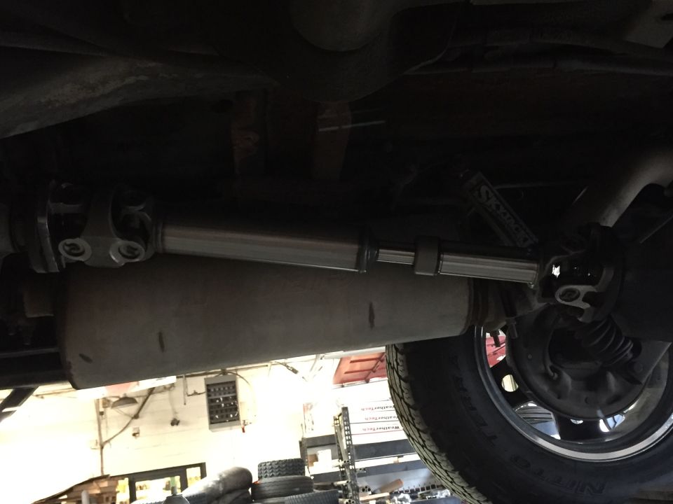 Underside view of a driveshaft and exhaust pipe, with a tire and brake drum visible