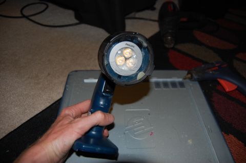 1994 Ford Bronco - A hand holds a blue and black Philips LED flashlight with three illuminated bulbs over a gray electronic device. In the background, a black…