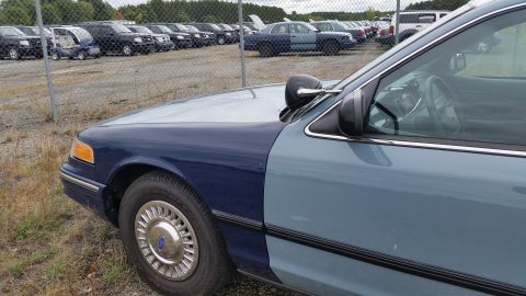 1991 Ford LTD Crown Victoria - Photograph of the front fender, wheel, and headlight of a two-tone Crown Victoria in a storage lot, not a technical document.