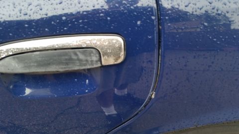 1991 Ford LTD Crown Victoria - Photograph of a chrome exterior door handle on a rain-beaded blue door, not a technical document.