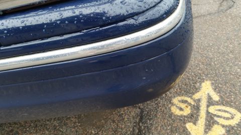 1991 Ford LTD Crown Victoria - Photograph of the rear bumper and chrome trim of a wet blue car above a parking-lot arrow, not a technical document.