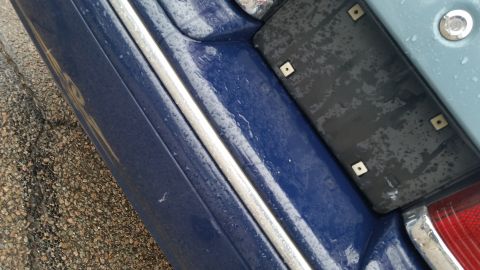 1991 Ford LTD Crown Victoria - Photograph of the rear license-plate bracket, taillight, and bumper of a blue car, not a technical document.