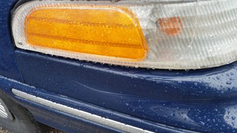 1991 Ford LTD Crown Victoria - Photograph of an amber turn-signal and clear corner lamp on the front bumper of a blue car, not a technical document.