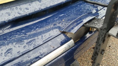 1991 Ford LTD Crown Victoria - Photograph of a separated body molding and panel gap on a rain-covered blue car, not a technical document.