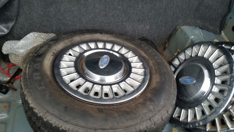 1991 Ford LTD Crown Victoria - Photo of a spare tire and Ford hubcaps in a trunk, not a technical document.