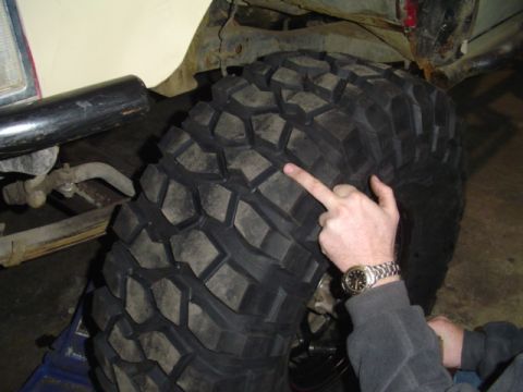 1993 Ford Bronco - A person points to the aggressive tread pattern of a large off-road tire mounted on a vehicle.