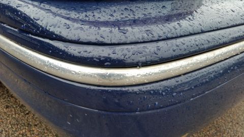 1991 Ford LTD Crown Victoria - Close-up photograph of a blue bumper and chrome trim with water beading, not a document.