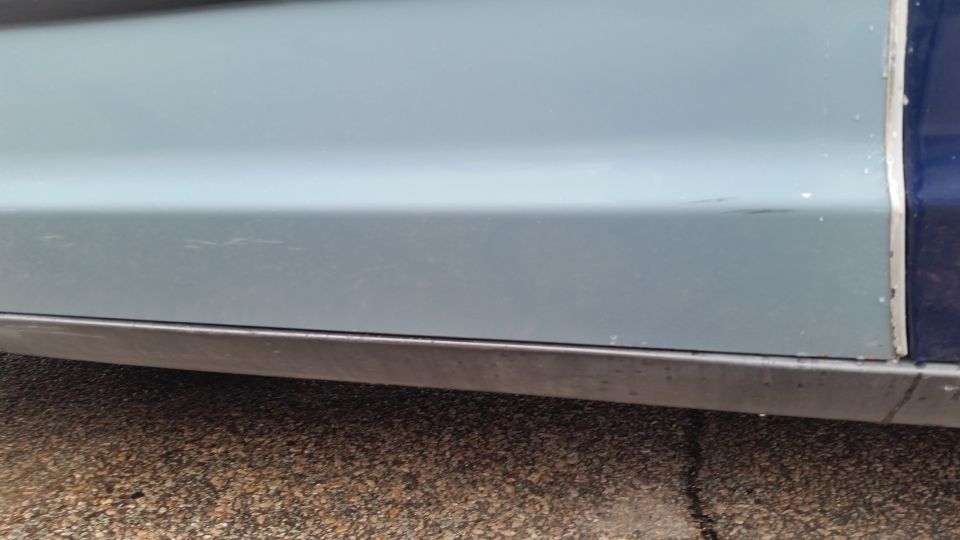Close-up of a light blue lower door and rocker panel of a sedan
