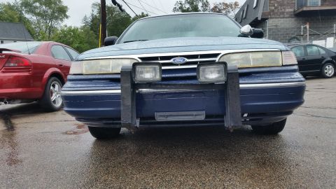 1991 Ford LTD Crown Victoria - A blue Ford Crown Victoria with a push bar is parked outside on a rainy day next to other vehicles.