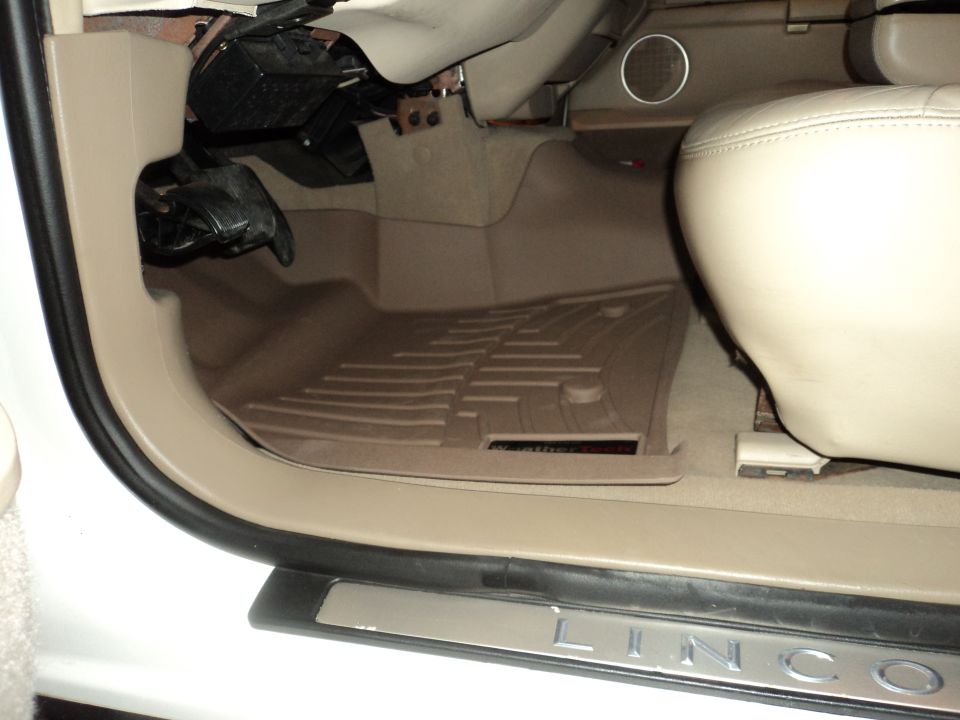Car interior showing driver's side floor with all-weather mats and part of the driver's seat. Text 'LINCOLN' visible on the door sill